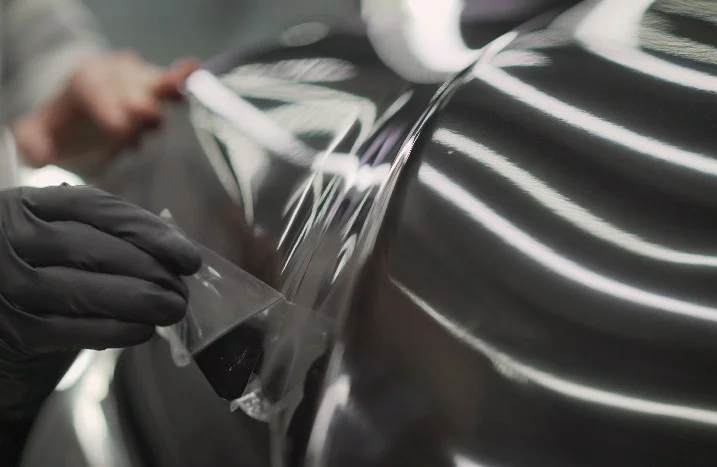 Eine Person in schwarzen Handschuhen entfernt eine Schutzfolie von einer glänzenden Oberfläche.