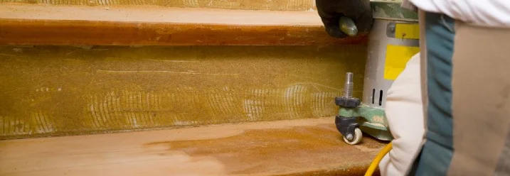 Person schleift Holztreppe mit Schleifmaschine