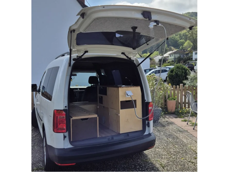 Ein weißer Van mit geöffnetem Kofferraum, der als Wohnmobil ausgebaut ist.