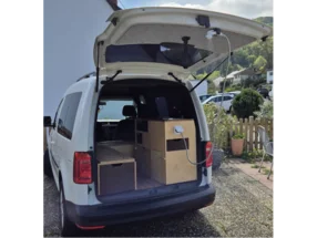 Ein weißer Van mit geöffnetem Kofferraum, der als Wohnmobil ausgebaut ist.
