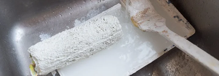 Farbrolle und Pinsel werden in einem Waschbecken gereinigt