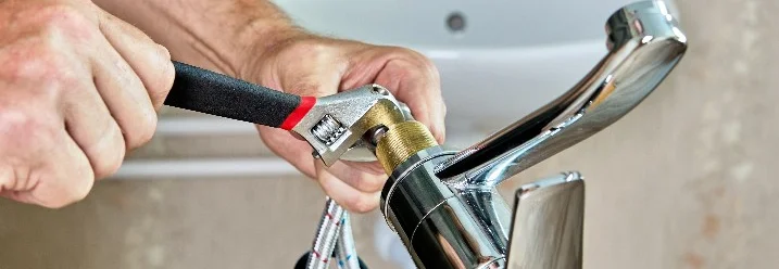 Person montiert einen Wasserhahn mit Schraubenschlüssel.