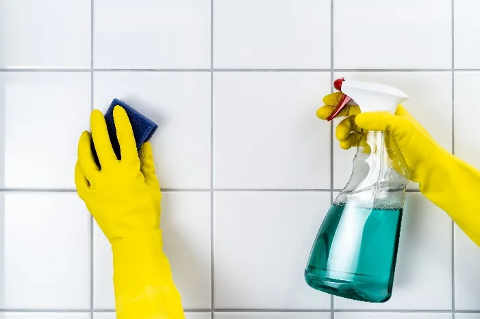 Hände mit Schwamm und Sprühflasche putzen Fliesen