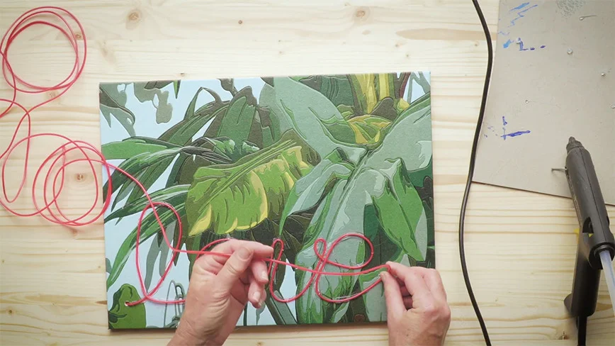 Hände formen Schriftzug mit roter Schnur auf Leinwand