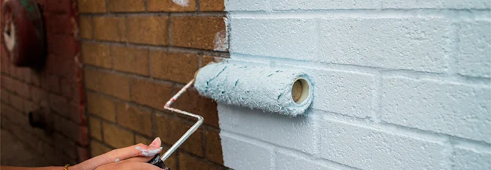 Person streicht eine Ziegelmauer weiß