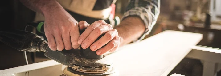 Person schleift Holzbrett mit Schleifmaschine
