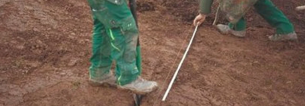 Zwei Personen messen matschigen Boden mit Zollstock und Spaten ab.