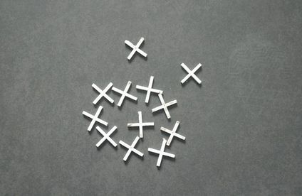 Fliesenkreuze: Unterstützung beim Fliesen legen Weiße Fliesenkreuze liegen auf dunkelgrauem Untergrund.