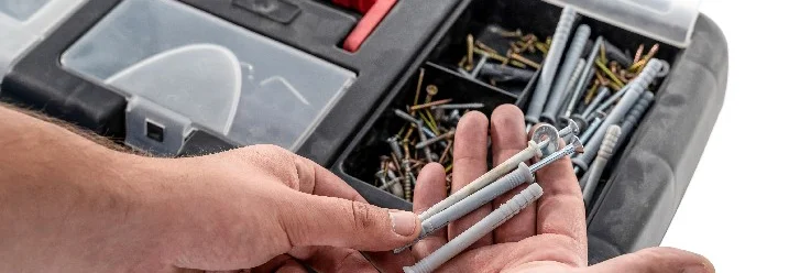 Hand hält Dübel über Werkzeugkasten