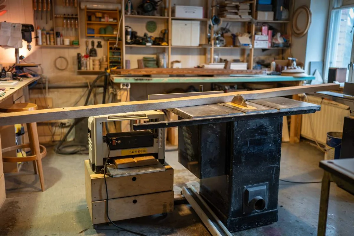 Tischkreissäge in einer Holzwerkstatt umgeben von Regalen mit Werkzeugen.