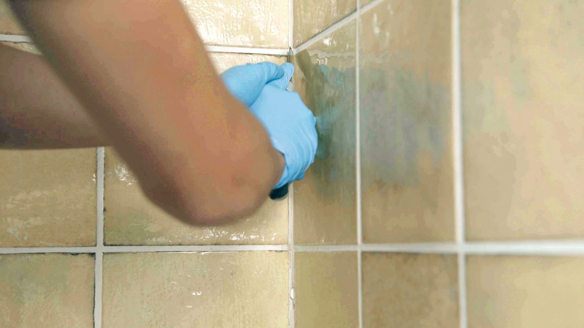 Mit einem Cuttermesser werden alte Silikonfugen zwischen Wandfliesen entfernt.