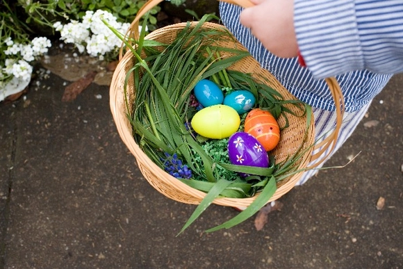 Ein Kind hält einen Osterkorb gefüllt mit bunten Eiern und Gras.