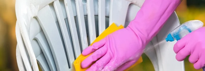 Hand reinigt Gartenstuhl mit Schwamm