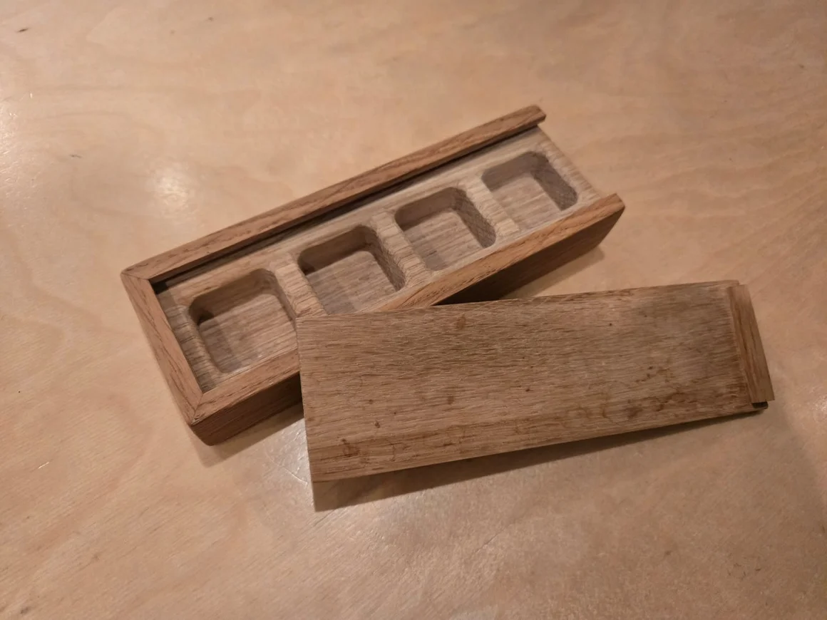Eine kleine, offene Holzschachtel mit vier Fächern und daneben liegendem Deckel.