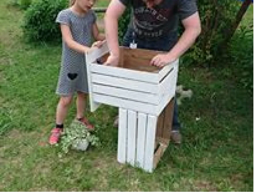 Zwei Personen bauen ein Hochbeet aus Holz zusammen.