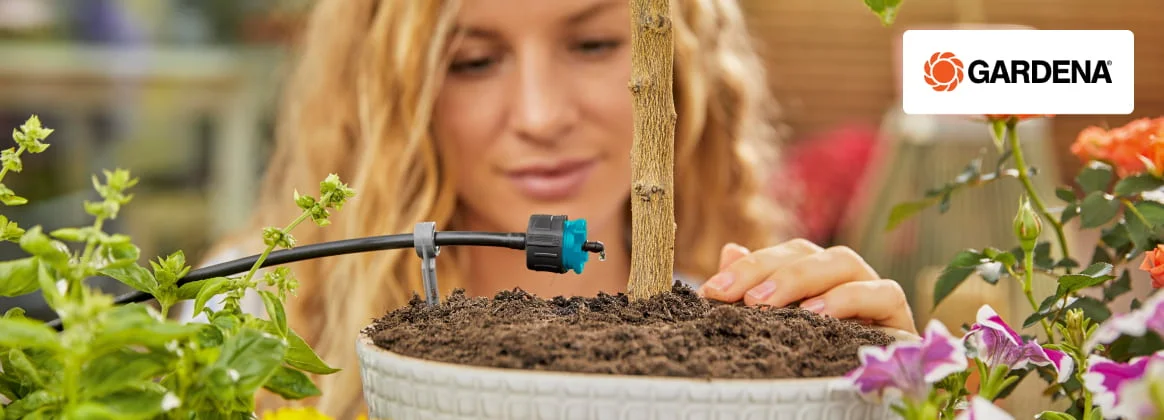 Eine Person installiert eine Tropfbewässerung der Marke Gardena für eine Pflanze in einem Topf.