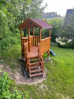 Ein unfertiges Spielgerüst aus Holz steht in einem Garten.