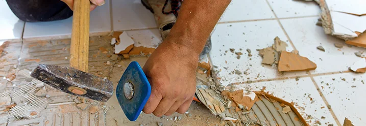 Person entfernt Fliesen mit Hammer und Meißel