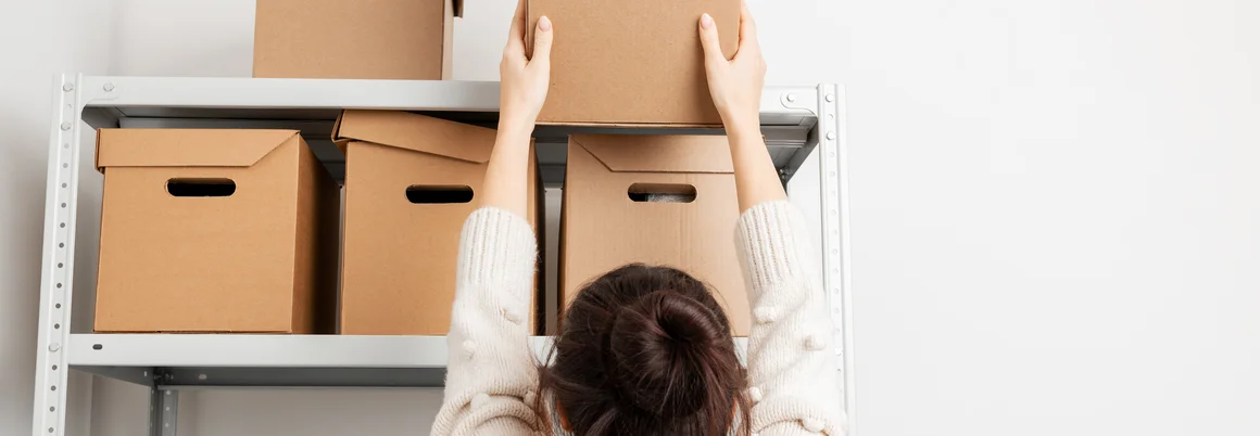 Person räumt Karton in Regal ein