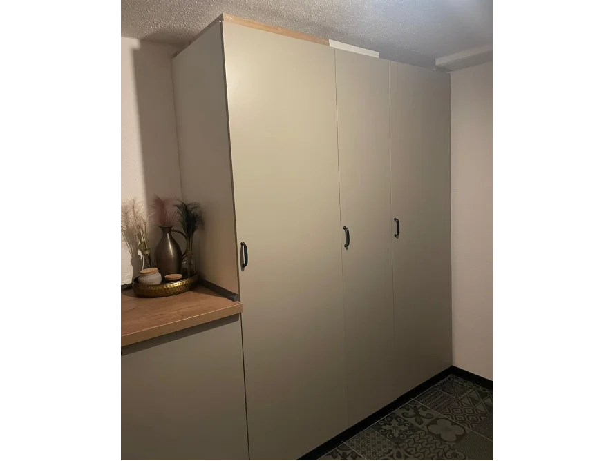 Ein hochgebauter, beigefarbener Schrank mit schwarzen Griffen.