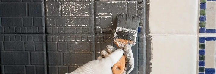 Hand trägt Farbe mit Pinsel auf Fliesen auf