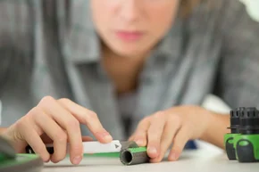 Person schneidet Schlauch mit einem Cuttermesser.