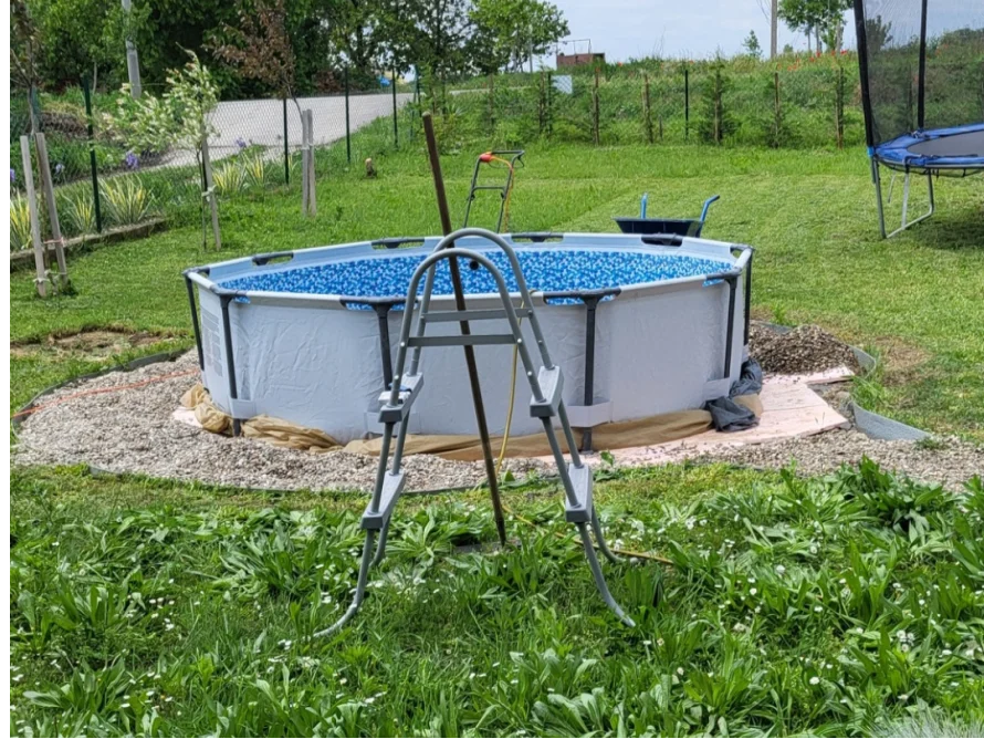 Ein Aufstellpool mit Leiter wird in einem Garten auf einer Kiesfläche aufgebaut.