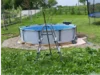 Ein Aufstellpool mit Leiter wird in einem Garten auf einer Kiesfläche aufgebaut.
