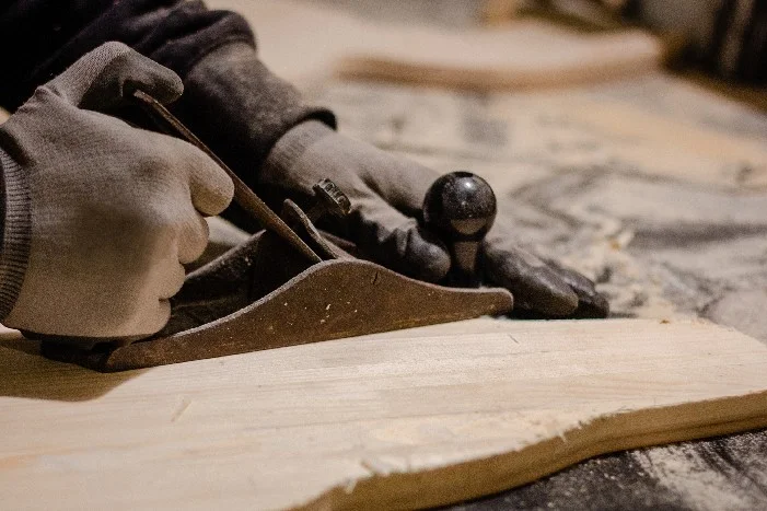 Person hobelt Holzbrett mit Hobel