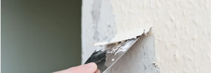 Hand entfernt Farbreste mit Spachtel von Wand