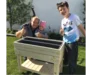 Drei Personen stehen hinter einem Hochbeet aus Holz.