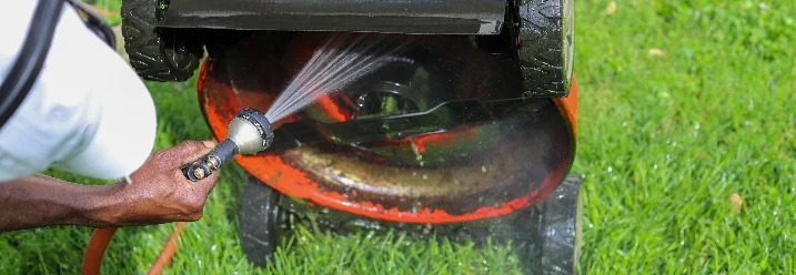Person reinigt Rasenmäher mit Schlauch.