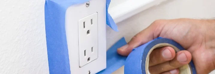 Person klebt Steckdose mit Malerband ab