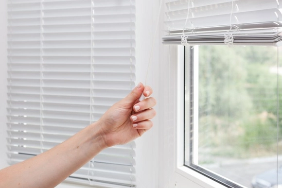 Eine Hand bedient die Schnur einer weißen Jalousie.
