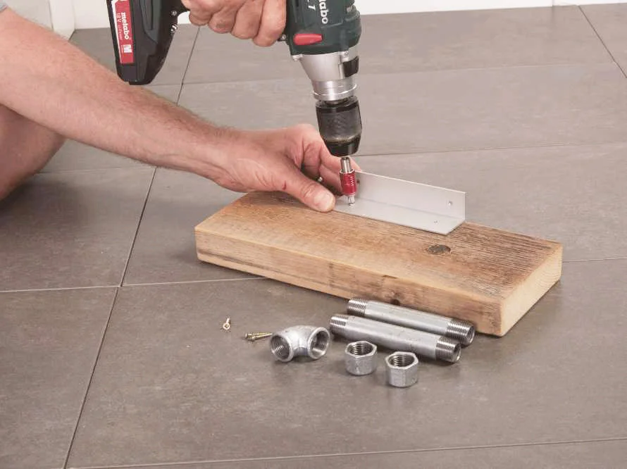Person befestigt Metallwinkel an Holzbrett