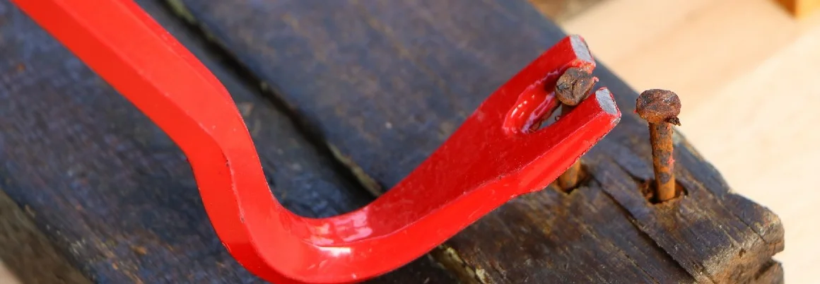 Ein roter Nagelzieher entfernt einen Nagel aus einem Holzbrett.