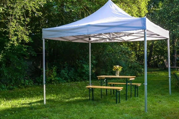 Weißer Pavillon mit Bierzeltgarnitur auf einer Wiese im Garten.