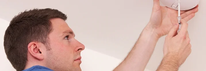 Person montiert Rauchmelder mit Schraubendreher