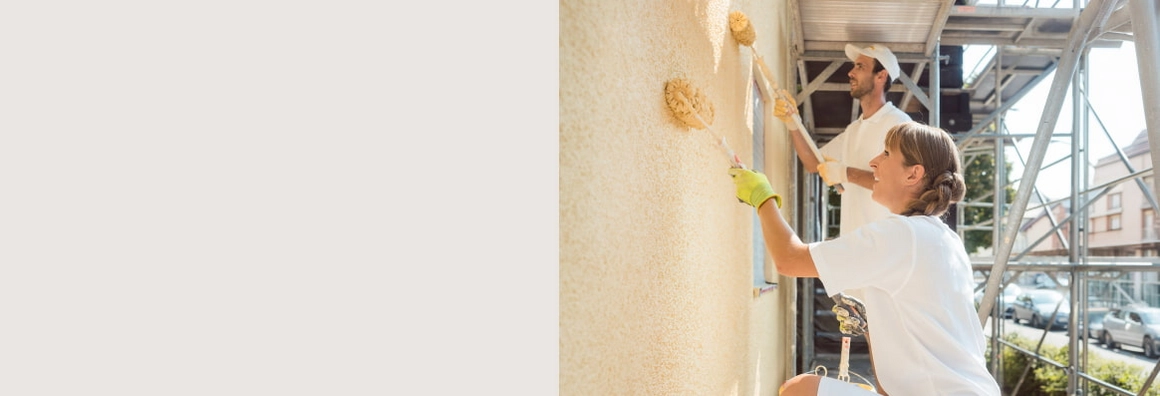 Zwei Personen streichen eine Hausfassade mit Strukturrollern.