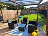 Eine überdachte Terrasse mit schwarzen Gartenmöbeln und Blick auf einen grünen Rasen.