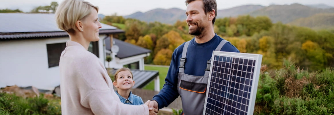 Zwei Personen geben sich neben einem Photovoltaik-Element die Hand