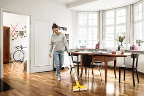 Person reinigt Holzboden mit Sprühreiniger.