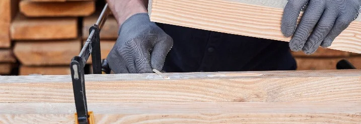 Person verklebt Holzbalken mit Schraubzwinge