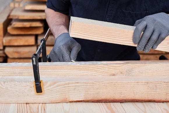 Person verklebt Holzbalken mit Schraubzwinge