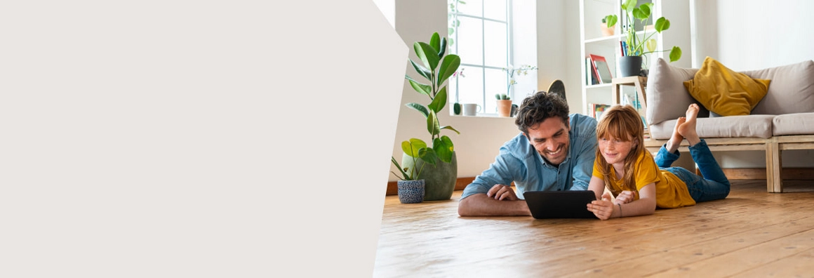 Kind und Mann liegen auf Holzboden mit Sofa im Hintergrund.