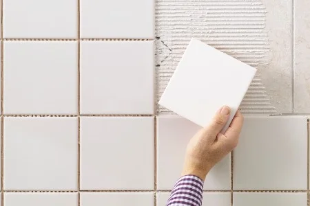 Hand befestigt Fliese an Wand