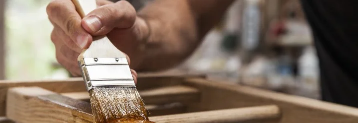 Person streicht Holz mit Pinsel