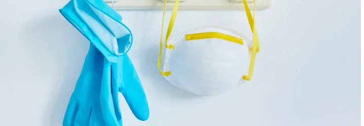 Ein Paar blaue Handschuhe und eine Atemschutzmaske hängen an einer Garderobe.
