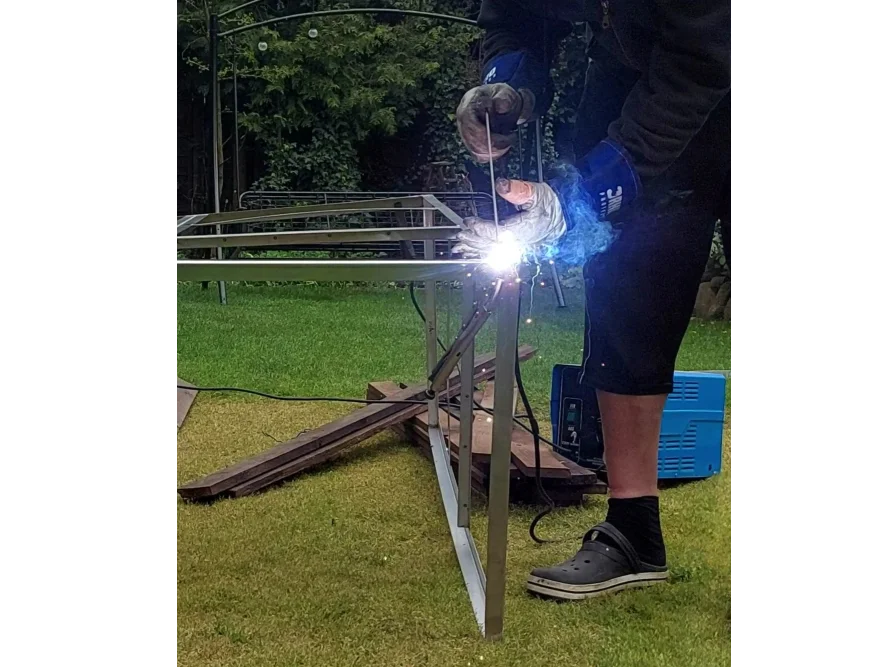 Person schweißt Metallrahmen im Garten