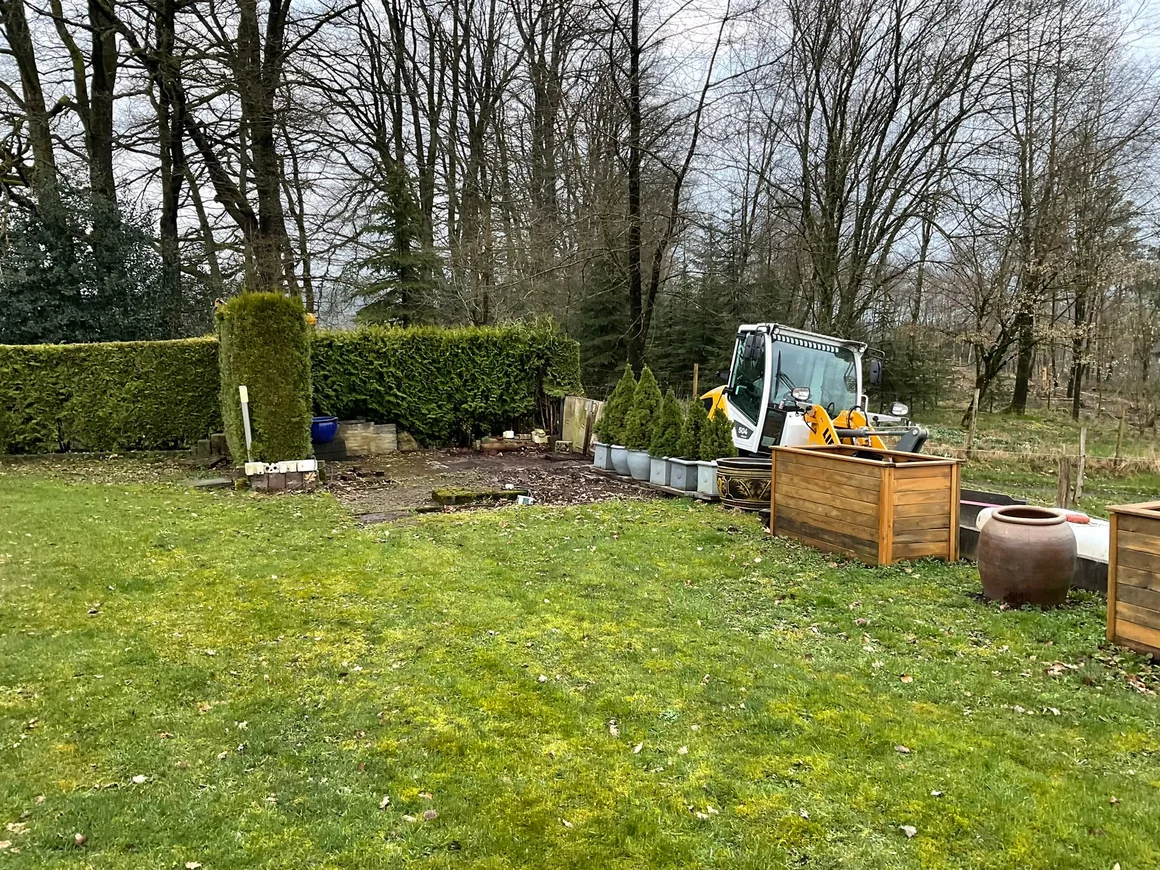 Ein kleiner Bagger steht bei Gartenarbeiten auf einer Rasenfläche.